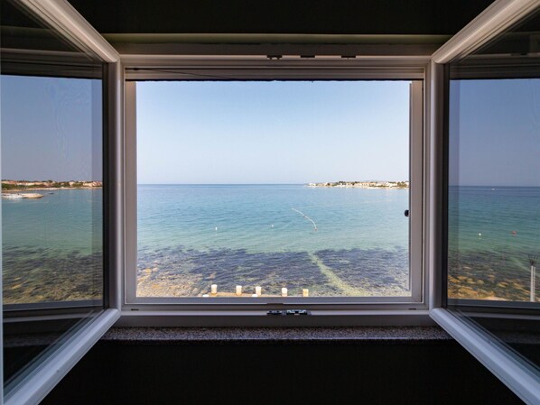 Blick durch ein Fenster auf das Meer und eine entfernte Küste.
