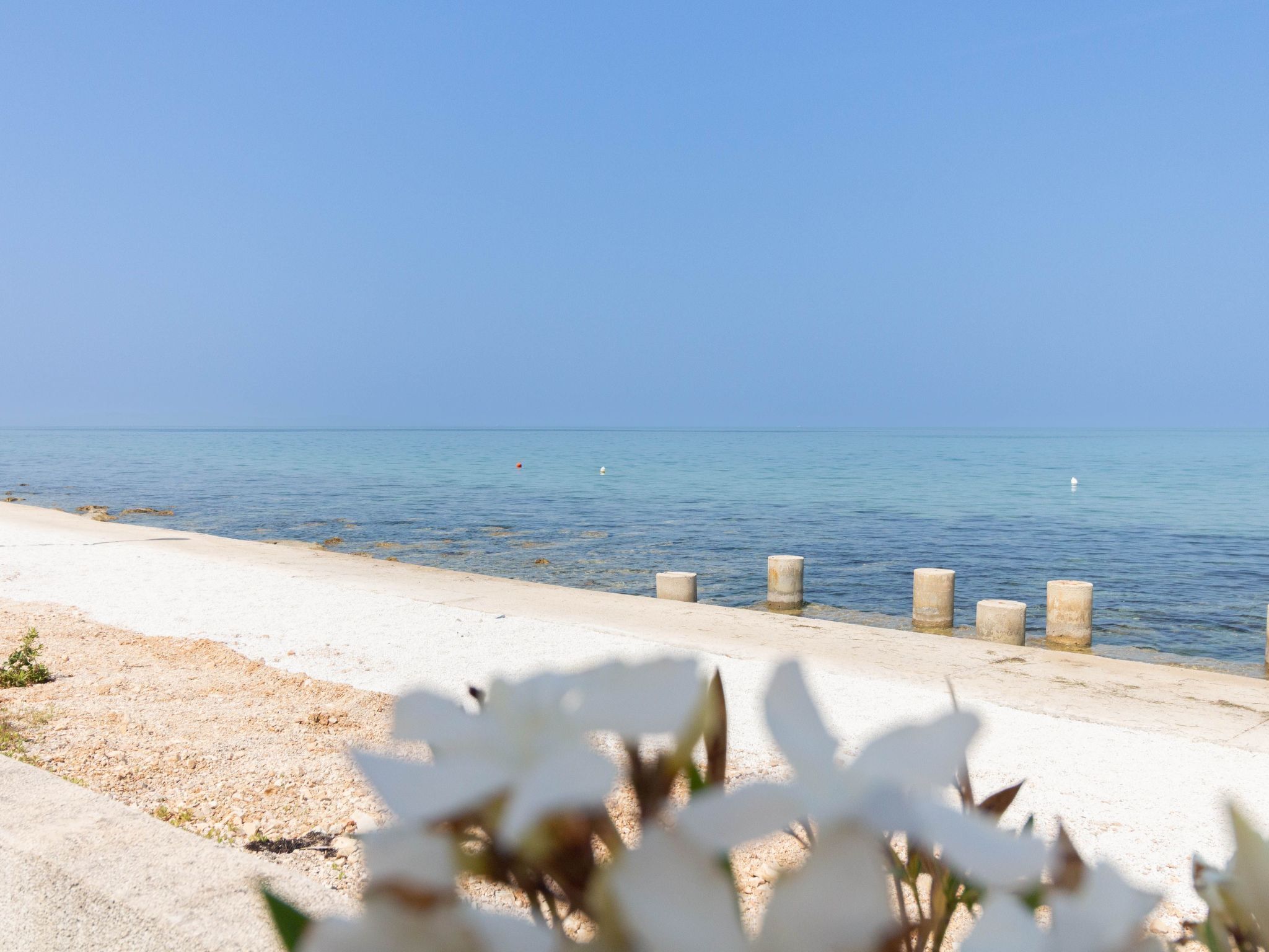 A beach with a concrete walkway and a clear view of the sea.