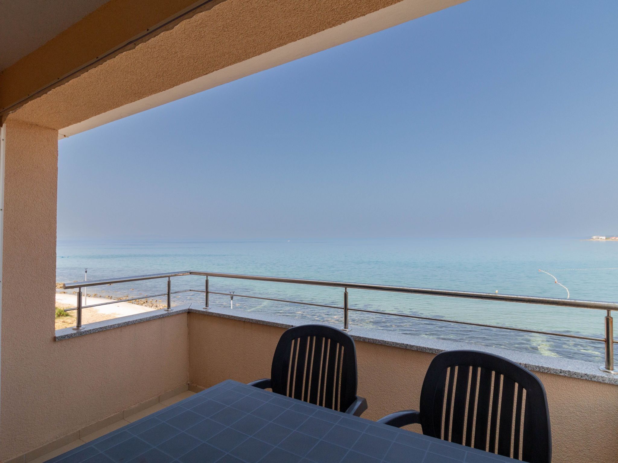 Varanda com mesa e cadeiras, com vista para uma praia e o mar.