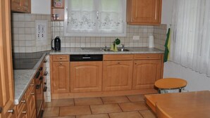 Une cuisine compacte avec des meubles en bois, un lave-vaisselle encastré, une fenêtre avec des rideaux et un pare-feu en carrelage.