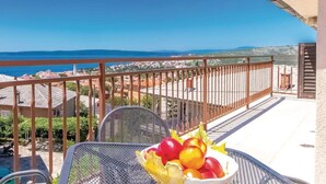 Ein Balkon mit einem Metalltisch und Stühlen, einer Obstschale und Blick auf das Meer und die Stadt.