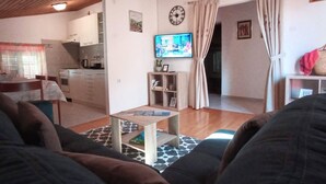 Ein Wohnzimmer mit einer Couch, einem Couchtisch, einem Fernseher und einer Küche im Hintergrund.