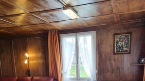 Une pièce chaleureuse avec un plafond en bois, une table ronde en bois entourée de chaises, un canapé rouge et une fenêtre avec des rideaux.