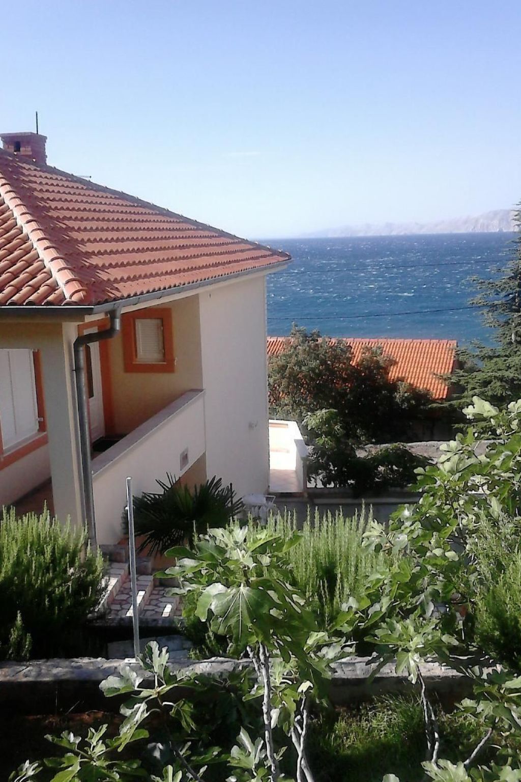 A house with a red-tiled roof, a white exterior, and a view of the sea.