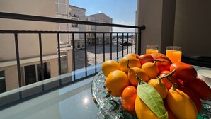 Un balcon avec une table en verre sur laquelle sont disposées des oranges et un verre de jus d’orange.