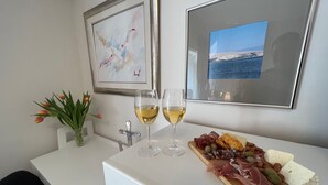 Un coin repas avec une table blanche, deux verres de vin blanc, une planche en bois sur laquelle sont disposés divers fromages et charcuteries, un vase de tulipes et deux tableaux encadrés accrochés au mur.