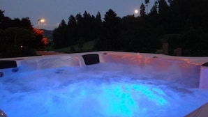 Un bain à remous avec un éclairage bleu, entouré d’arbres et avec une montagne en arrière-plan.