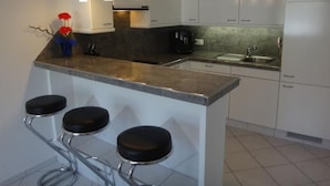 Une cuisine moderne avec des armoires blanches, un comptoir en granit et un îlot central intégré, agrémenté de tabourets de bar.