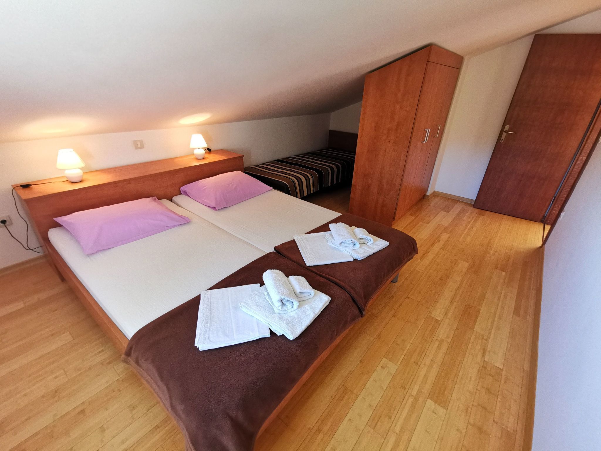 A twin room with two beds, wooden flooring, a wardrobe, and a bedside table with a lamp.