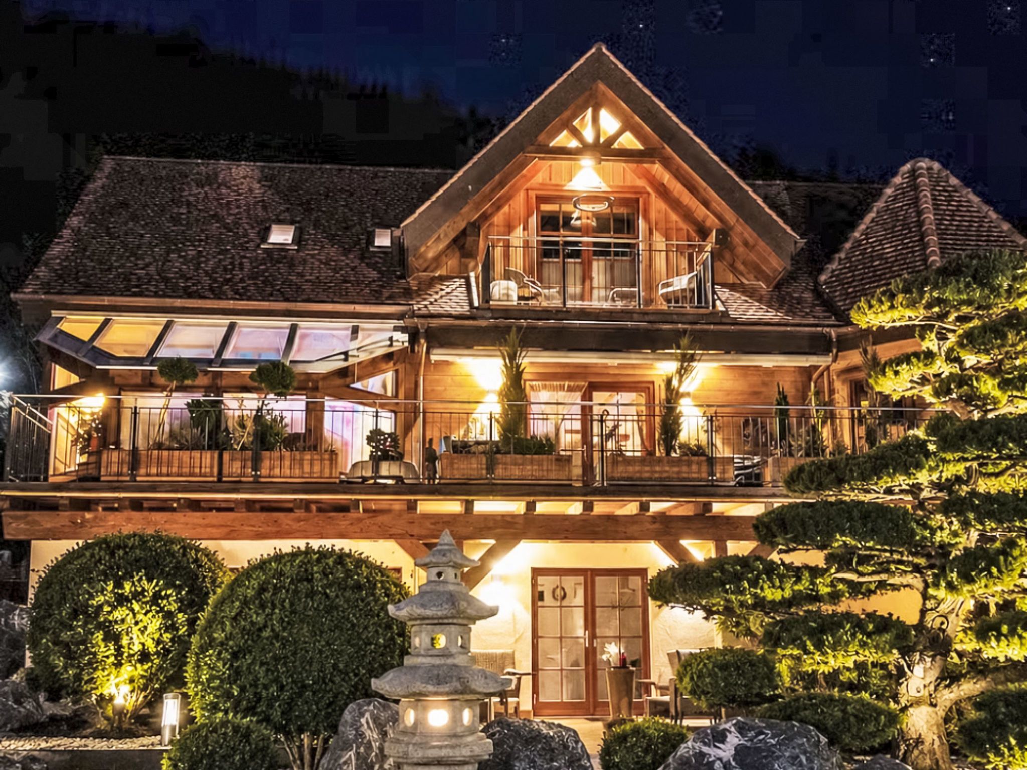 A two-story wooden house with a balcony, a stone lantern, and a well-maintained garden.