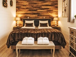 Ein Schlafzimmer mit einem hölzernen Kopfstück, zwei Nachttischen mit Lampen, einem großen Bett mit einer dunkel gemusterten Bettdecke und einer Bank mit Handtüchern.