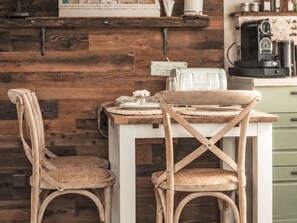 A rustic kitchen with wooden walls, a white table, two wicker chairs, and a coffee machine. - Seelenholz by Interhome (Herbetswil)