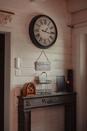 A wall clock with Roman numerals, a welcome sign, a small shelf with books, and a decorative wooden cabinet. - Seelenholz by Interhome (Herbetswil)