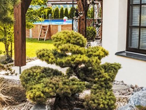 A well-maintained garden with a bonsai tree, a wooden deck, and a swimming pool in the background. - Seelenholz by Interhome (Herbetswil)