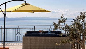 Ein Balkon mit einer Rattan-Couch, einem gelben Sonnenschirm und Meerblick.