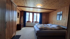 A wooden-paneled room with a bed, a dresser, and a window with curtains. - Stöckli EG by Interhome (Bowil)