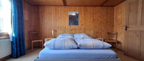 Une chambre à coucher aux murs lambrissés, avec un lit, deux tables de chevet et une fenêtre avec des rideaux.