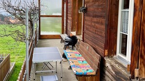 An outdoor patio with a table and bench, a grill, and a view of a green field. - Chalet Hulda by Interhome (Heimenschwand)