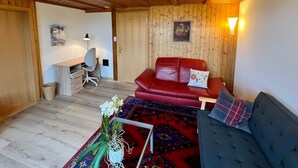 A cozy room with a red leather sofa, a blue sofa, a desk with a chair, and a small table with a vase of flowers. - Chalet Hulda by Interhome (Heimenschwand)
