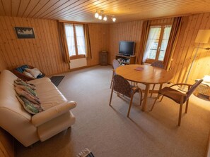 Ein gemütliches Zimmer mit Holzvertäfelung, einer Couch, einem Esstisch mit Stühlen und einem Fernseher.