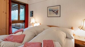 Habitació amb dos llits, una finestra amb cortines vermelles, un quadre a la paret i una làmpada a la tauleta de nit.