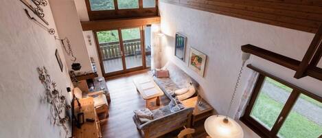 A spacious room with a wooden ceiling, large windows, a wooden dining table, and a cozy seating area.