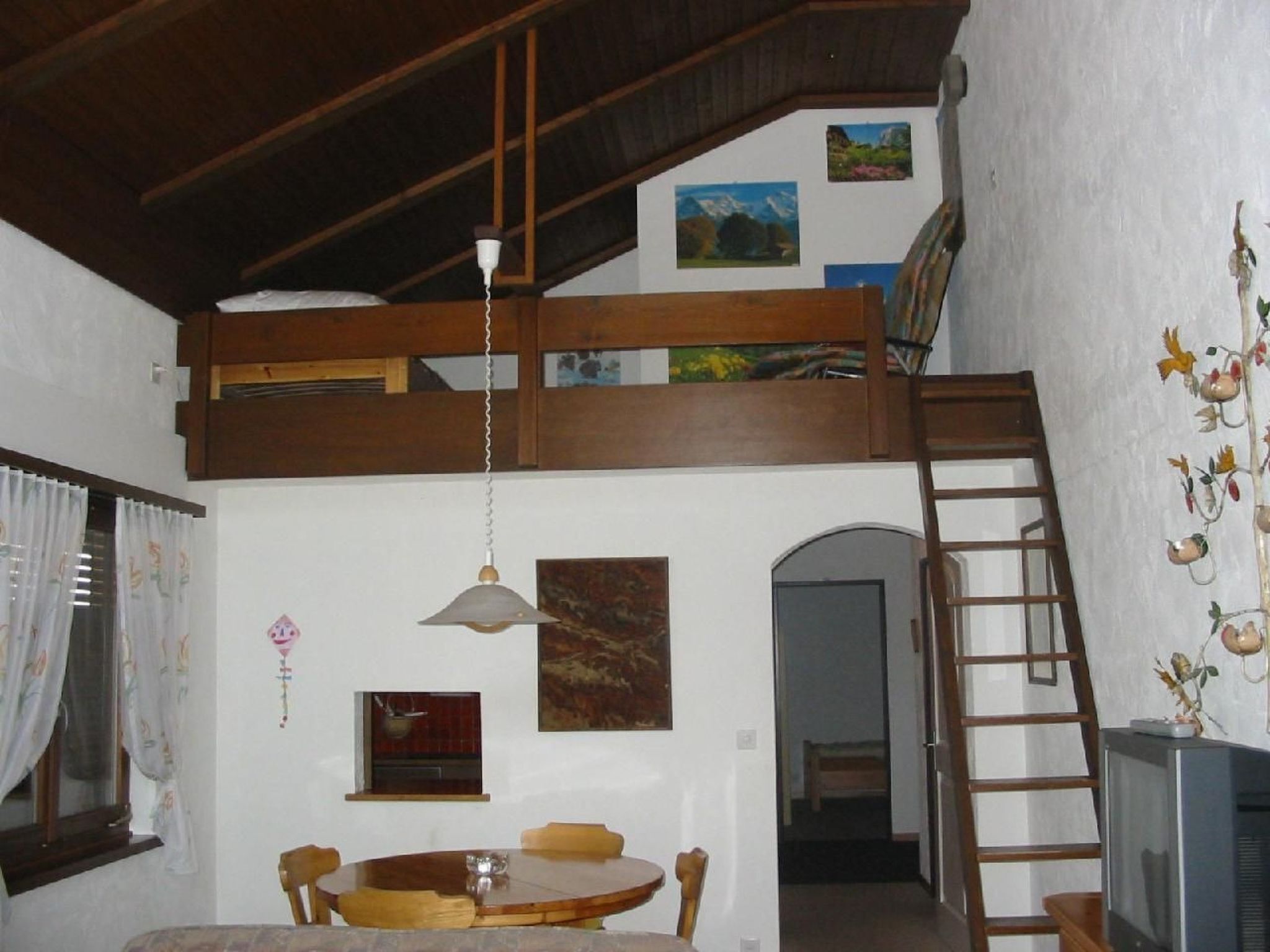 Une chambre à coucher aménagée en mezzanine avec un lit superposé, un coin repas avec une table ronde et un téléviseur.