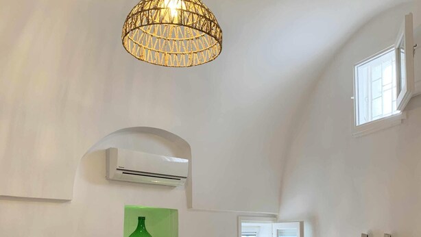 A bedroom with a wooden headboard, a bed with a green bedspread and two pillows, a hanging light fixture, an air conditioning unit, a green vase, and a ladder against the wall. - Biancostuni81, Le Piccole Case Bianche (Ostuni)