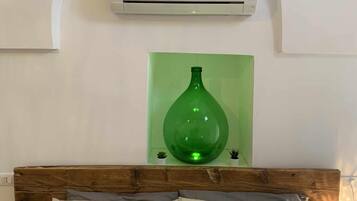 Un dormitorio con cabecera de madera, una cama con dos almohadas, un jarrón verde en un estante y un equipo de aire acondicionado en la pared.