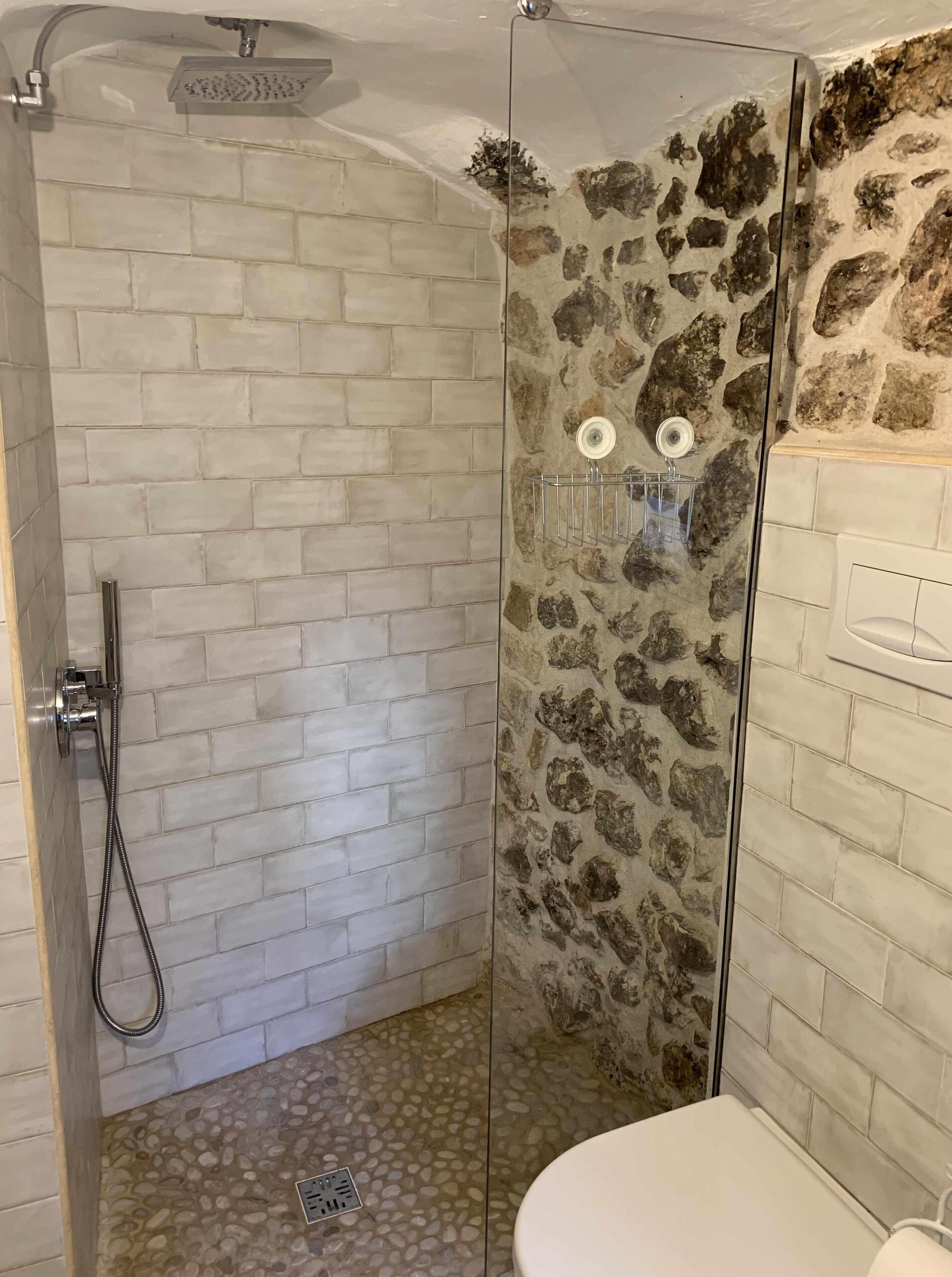 Una doccia con porta in vetro, parete rivestita di piastrelle e una sezione di parete in pietra.