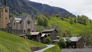 En kirke med et tårn og ur, omgivet af traditionelle bygninger og frodige grønne bakker.