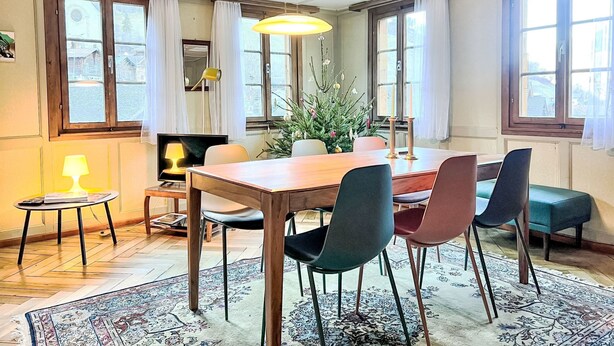 Et spiseområde med et træbord, stole, en lysekrone og et juletræ.