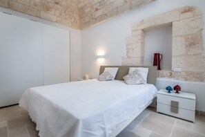 A bedroom with a bed, a nightstand, a wall-mounted lamp, and a stone wall. - Le Volte, Le Piccole Case Bianche (Ostuni)