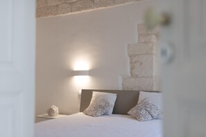 Ein Schlafzimmer mit einem Bett, zwei Kissen, einem Nachttisch, einer Wandleuchte und einer strukturierten Wand.