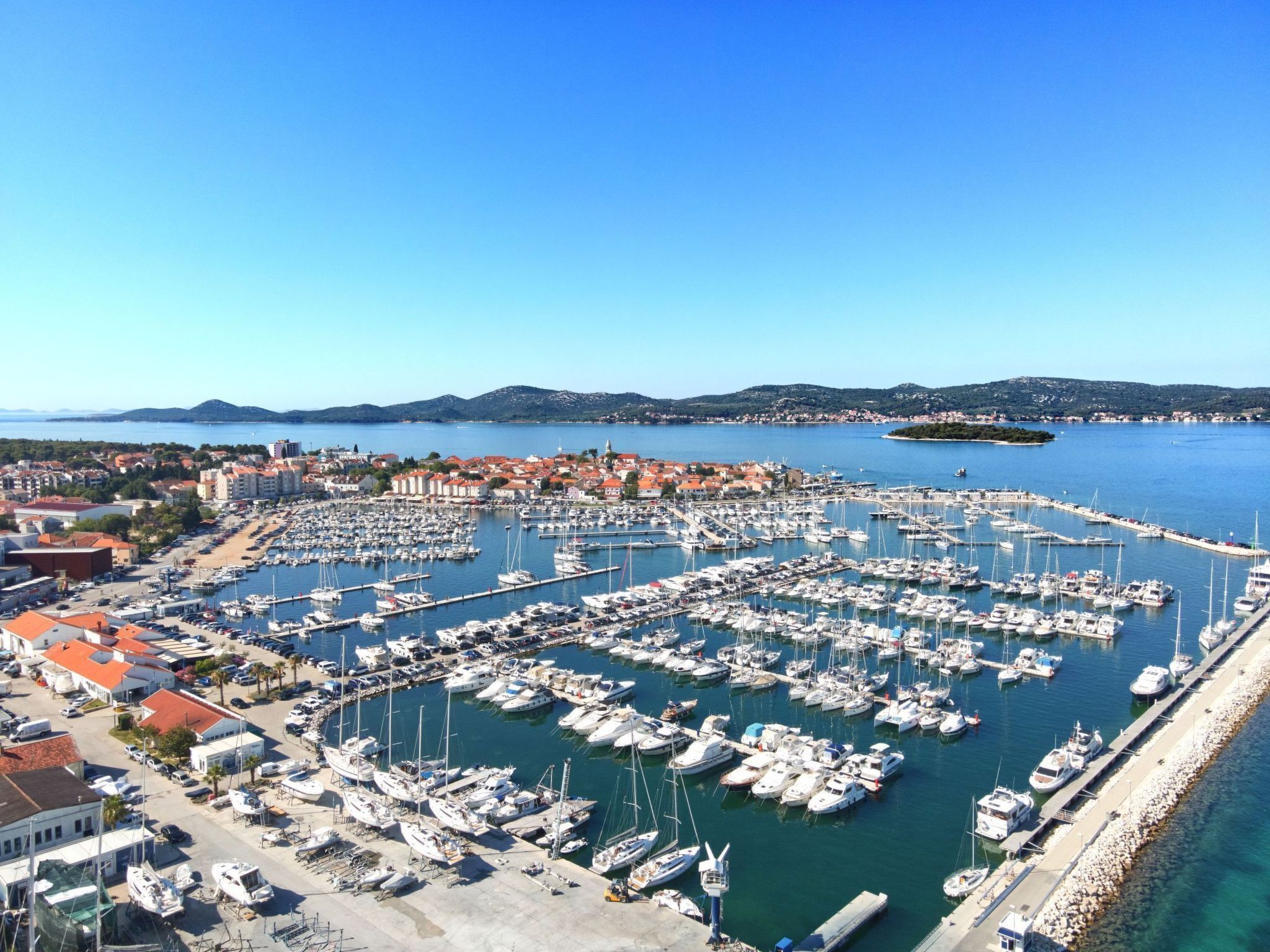 Un port de plaisance où de nombreux bateaux sont amarrés, entouré de bâtiments et surplombé par un ciel bleu clair.