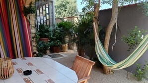 A round table with a tiled top, surrounded by wooden chairs, in a garden area with potted plants and a hammock. - Budget-Studio für zwei Personen by Interhome (Biograd na Moru)