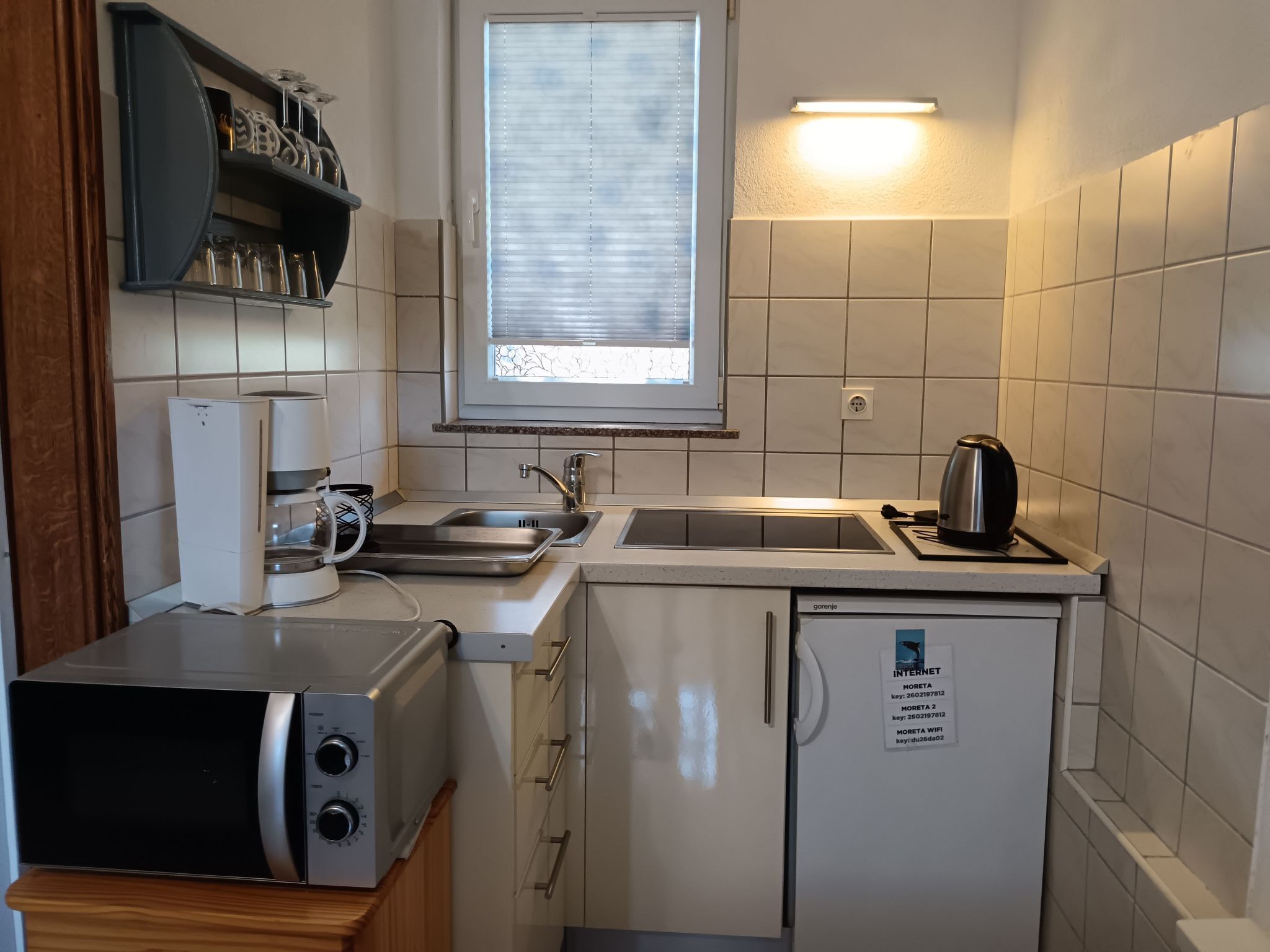 A compact kitchen with a microwave, a kettle, a sink, and a refrigerator.