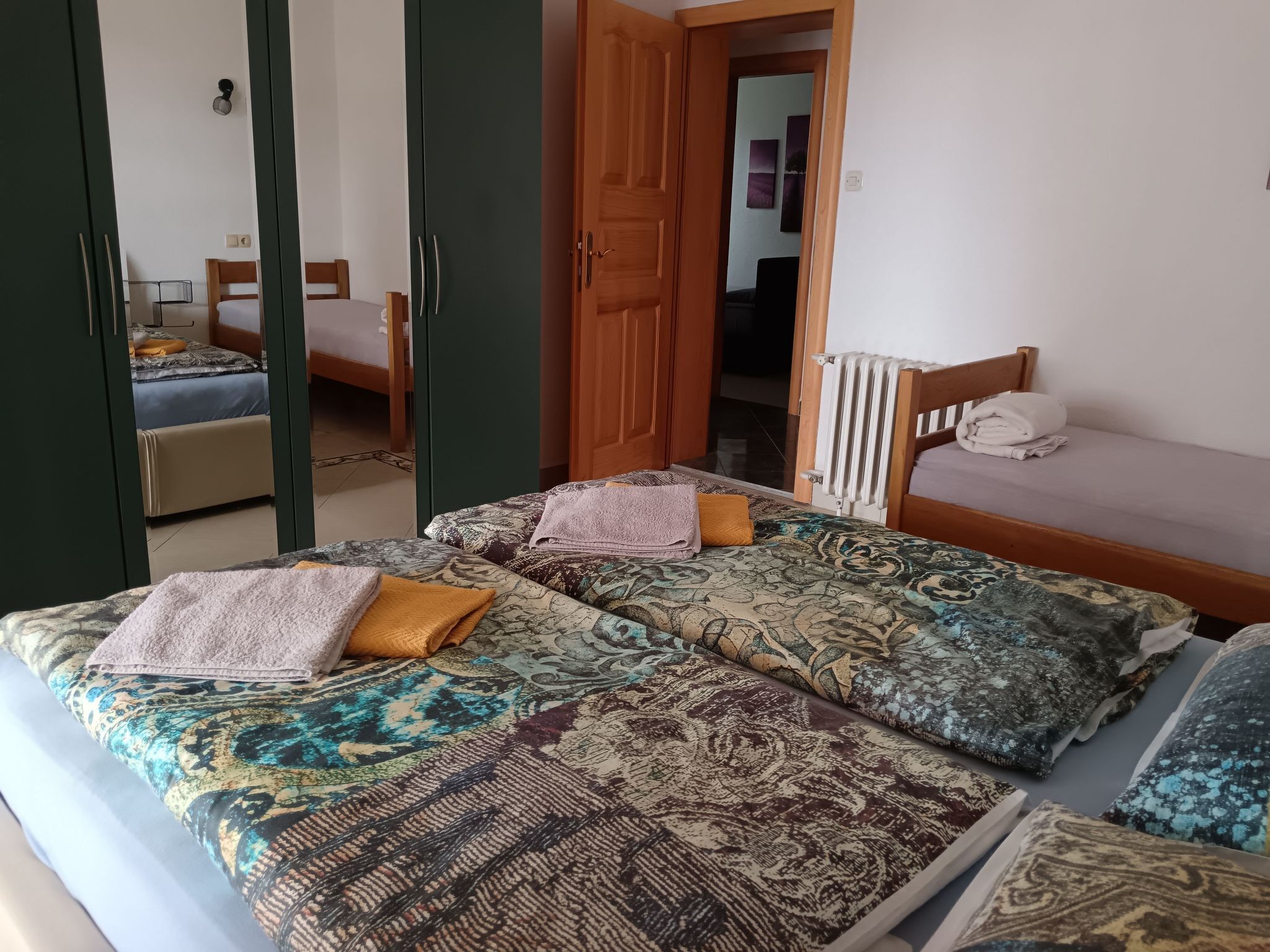 A room with two beds, each with patterned bedding and pillows. There is a wooden door and a radiator on the wall.