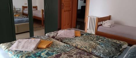 A room with two beds, each with patterned bedding and pillows. There is a wooden door and a radiator on the wall.