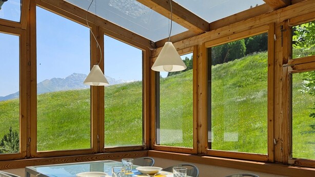Comedor con una mesa dispuesta para cuatro, ventanas amplias y vistas a una colina verde.