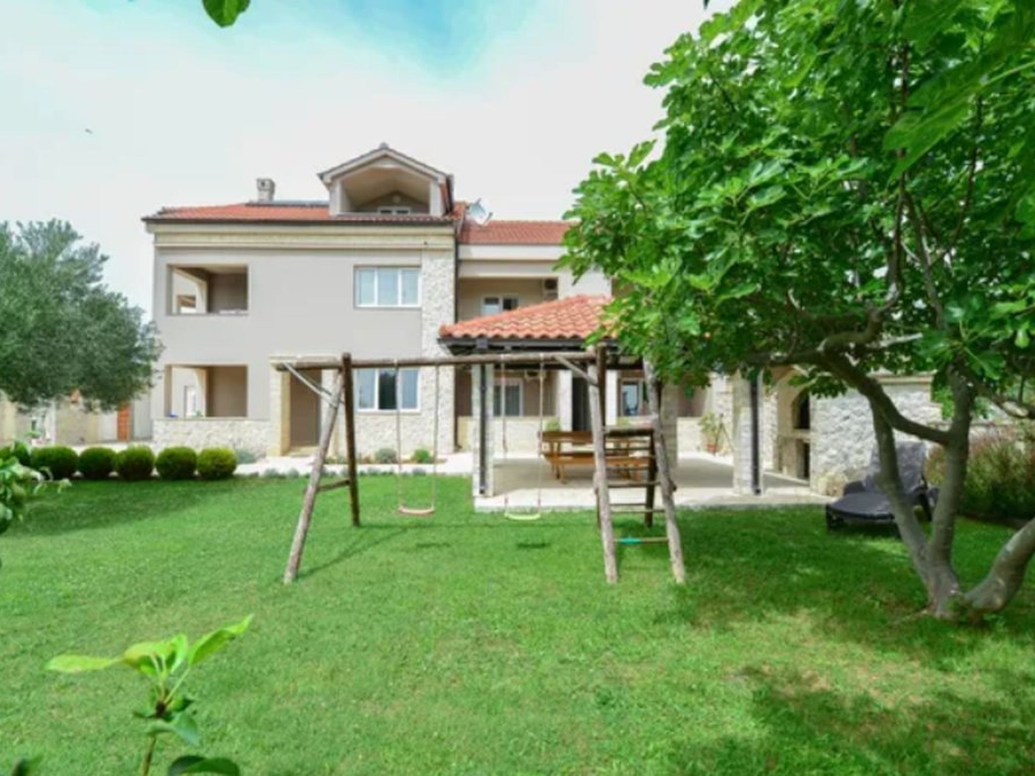 A two-story house with a red-tiled roof, a covered patio, and a swing set in the yard.