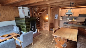 Ein gemütliches Blockhaushaus-Interieur mit Holzboden, einer Couch, einem Esstisch und einem Kamin.