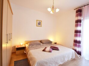 Ein Schlafzimmer mit einem Bett, Nachttischen, einer Lampe und einem Fenster mit Vorhängen.