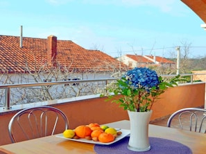 Ein Tisch mit Obstplatte und Blumen auf einem Balkon mit Blick auf Häuser.