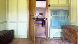 Una habitació amb una porta de fusta que dona a una zona de menjador, un armari de fusta i un moble amb porta de vidre.