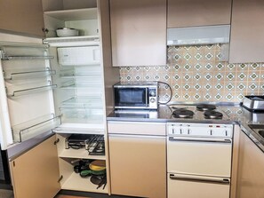 Une cuisine compacte équipée d’un four à micro-ondes encastré, d’une cuisinière et d’un réfrigérateur doté de plusieurs étagères.