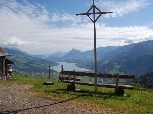 Un banco de madera con una cruz en el centro, con vistas a un valle con montañas y un lago.