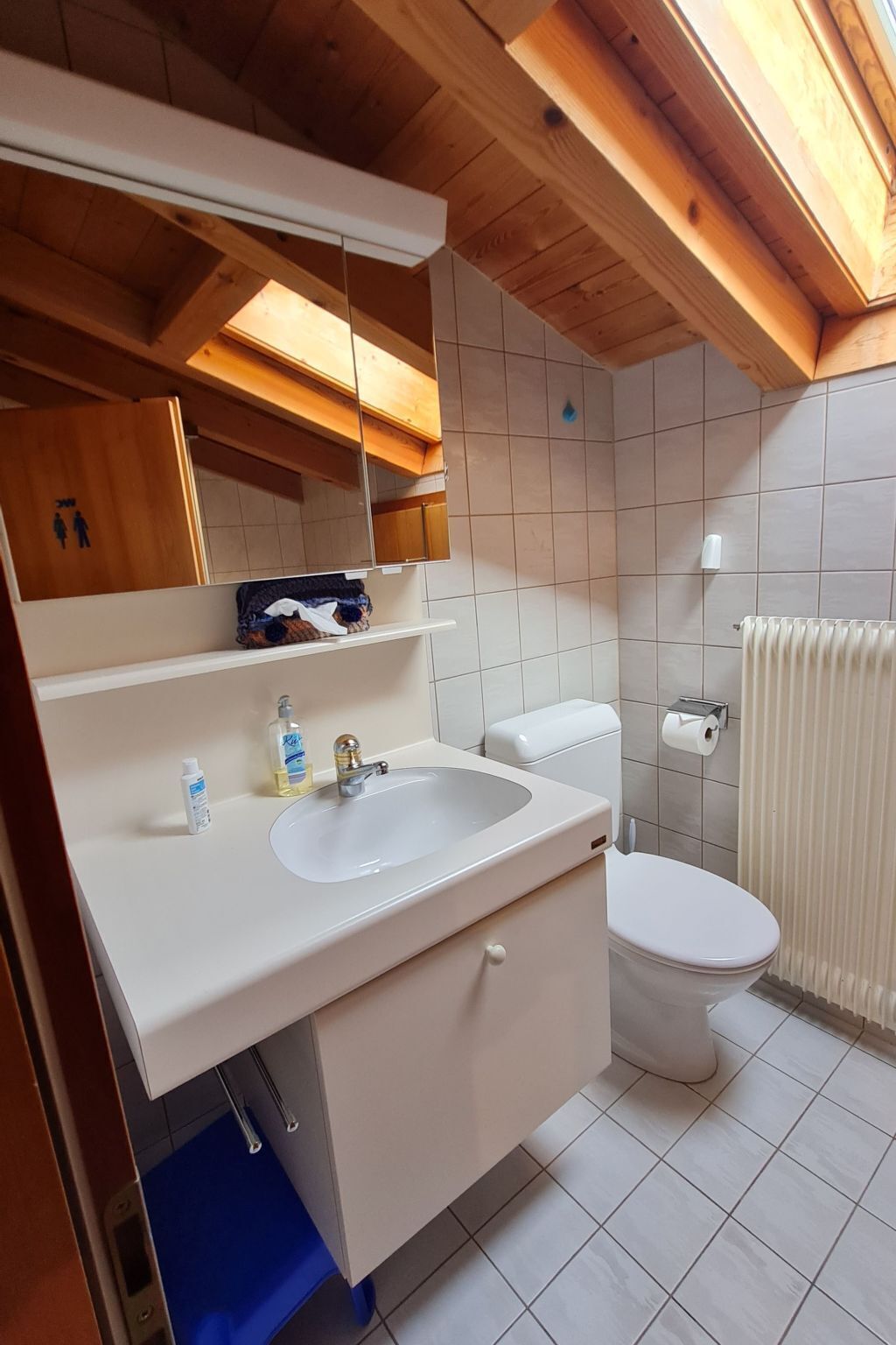 A bathroom with a white sink, mirror, and toilet. There is a towel rack and a toilet paper holder on the wall.