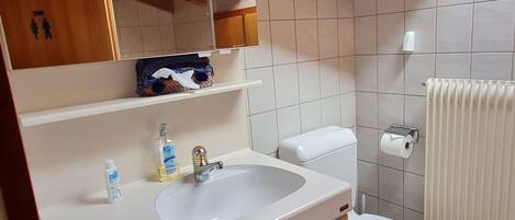 A bathroom with a white sink, mirror, and toilet. There is a towel rack and a toilet paper holder on the wall.