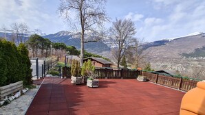 A red-tiled patio with potted plants, a wooden fence, and a mountain view. - Chalet Haus (bei Einfahrt grosser Nussbaum ) by Interhome (Leuk-Susten)